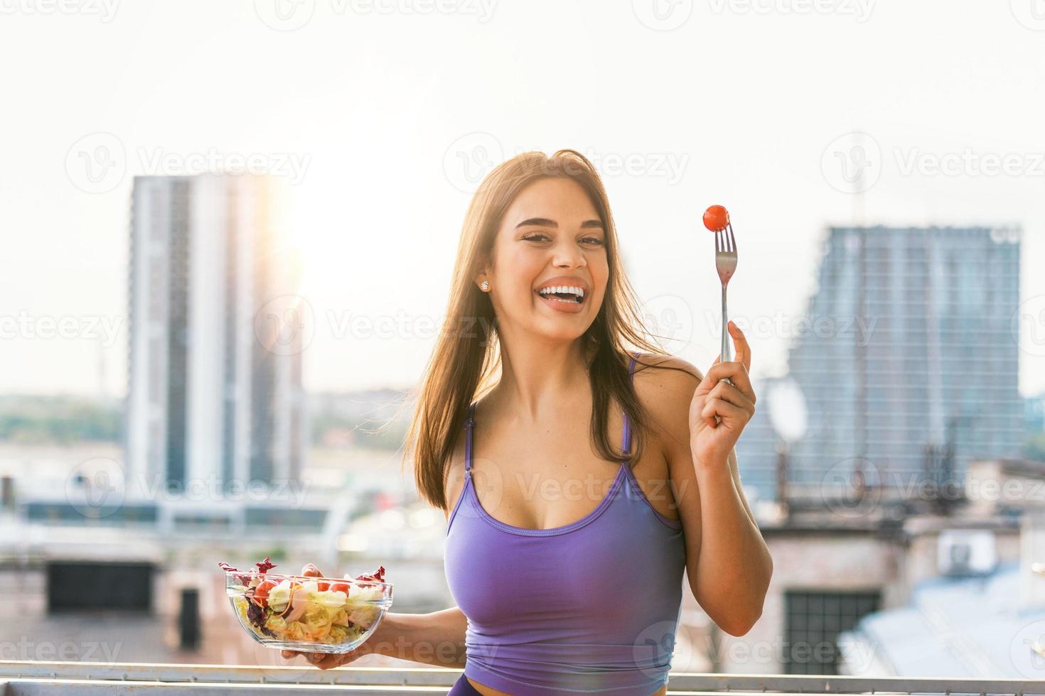 comenzando el día con comida saludable. mujer joven y hermosa disfrutando de una saludable ensalada con sol detrás de ella. dieta saludable. hermosa mujer sonriente comiendo ensalada vegetariana orgánica fresca. foto