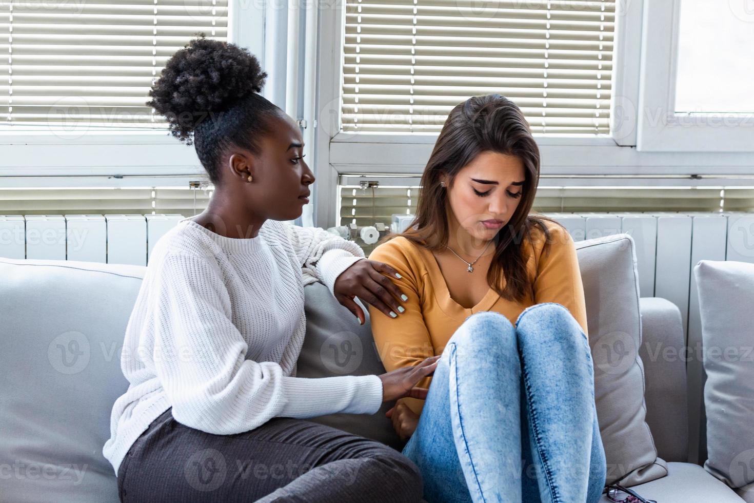 Sad girl and supporting friends trying to solve a problem. Two sad diverse women talking at home. Female friends supporting each other. Problems, friendship and care concept photo