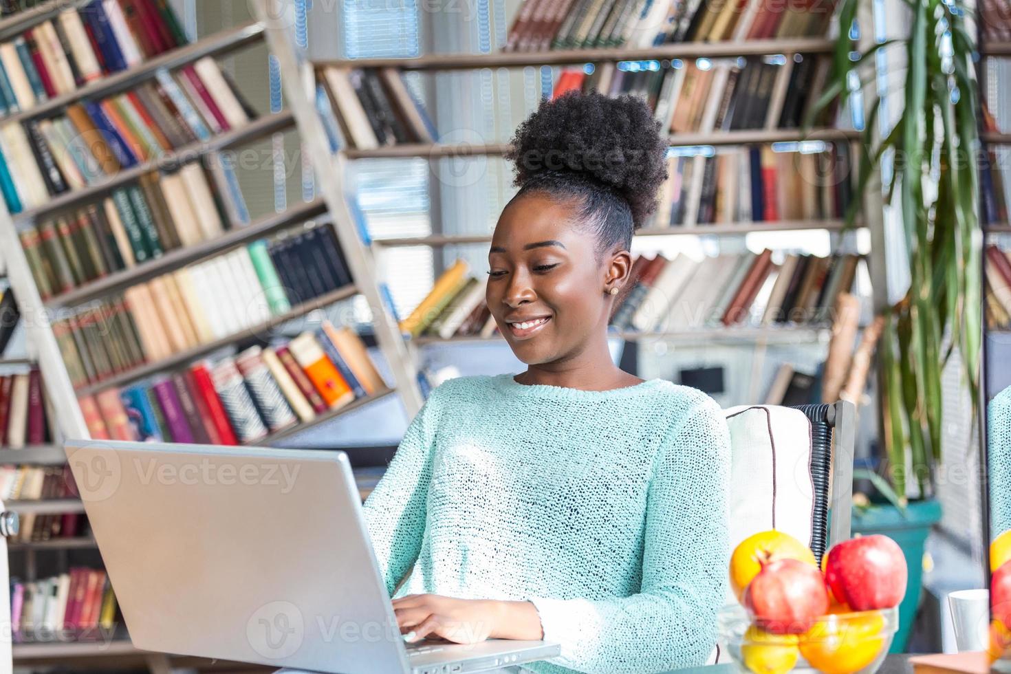 Young woman doing research work for her business. Smiling woman sitting on sofa relaxing while browsing online shopping website. Happy girl browsing through the internet during free time at home. photo