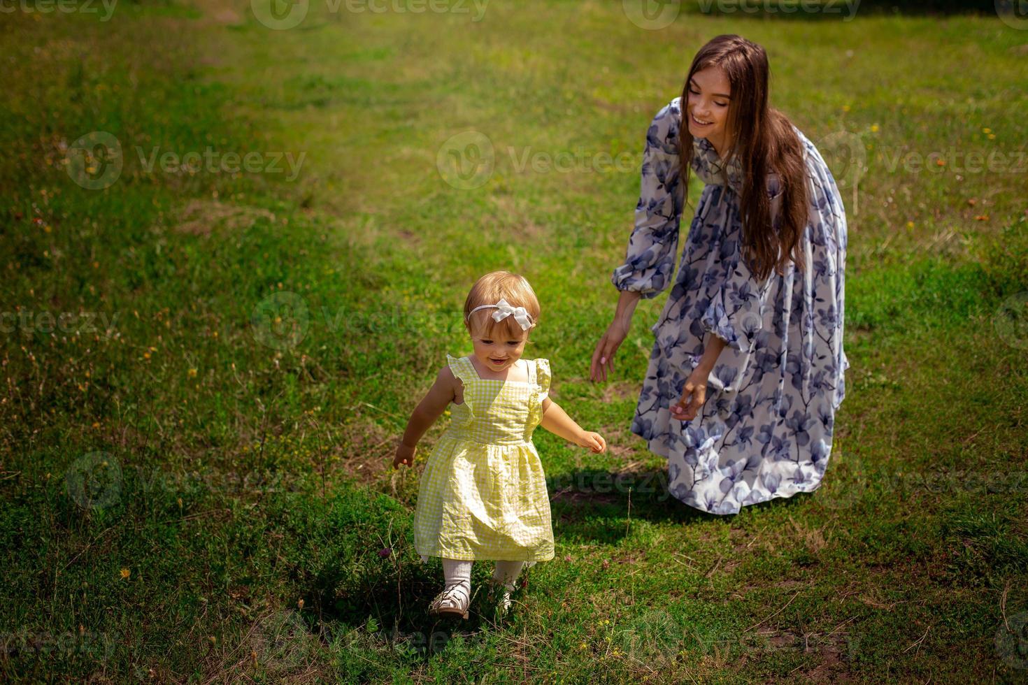 alegre joven madre juega con su pequeña hija en el jardín verde foto