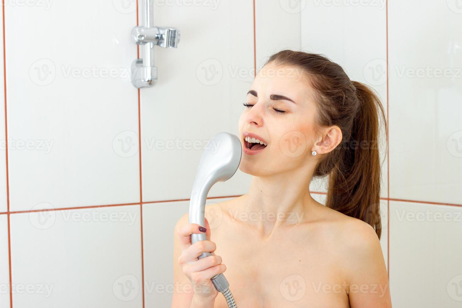chica joven divertida canta en la batidora en la ducha foto