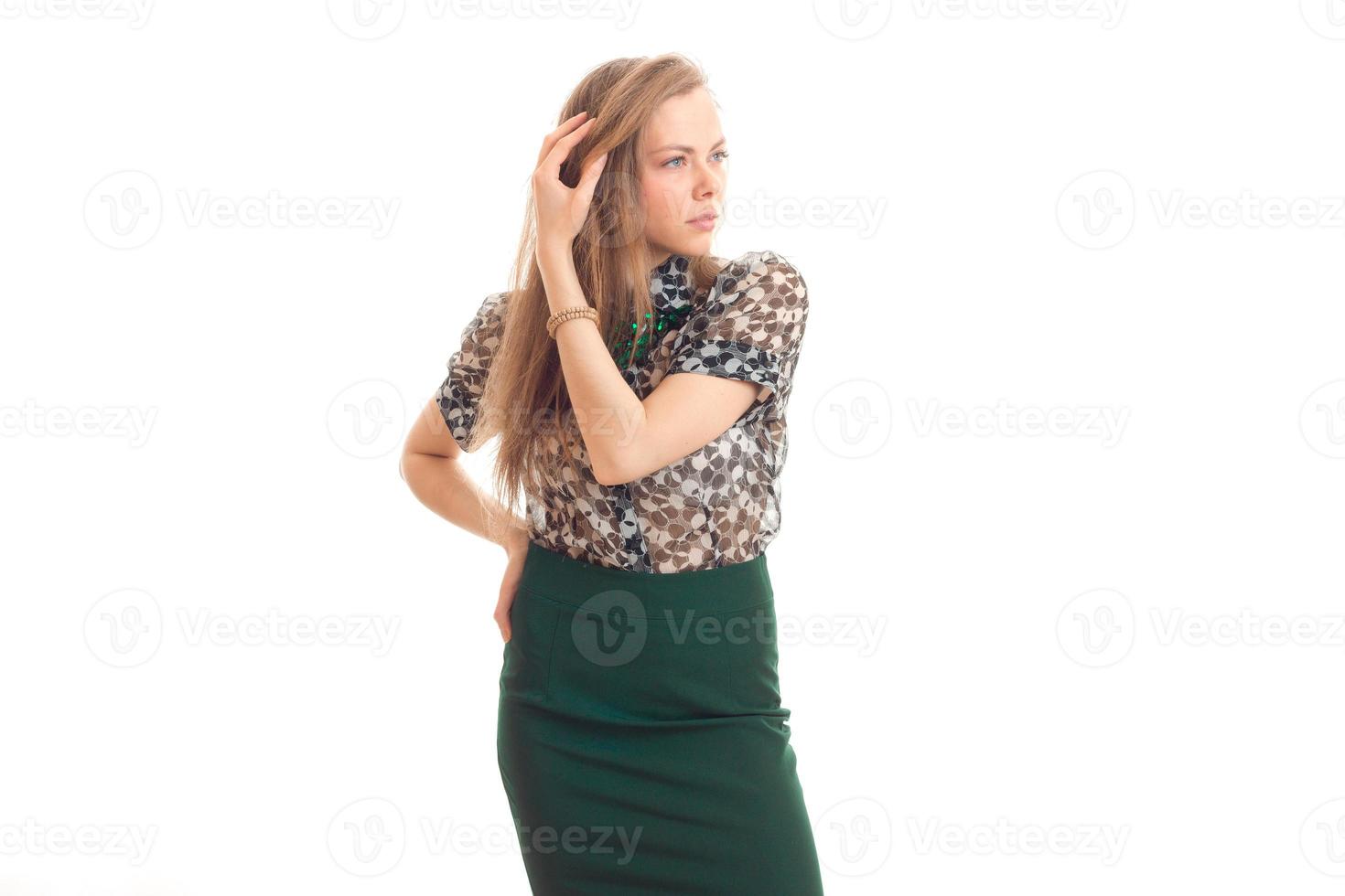 beautiful young girl in green skirt and blouse keeps an arm near hair and looks toward photo