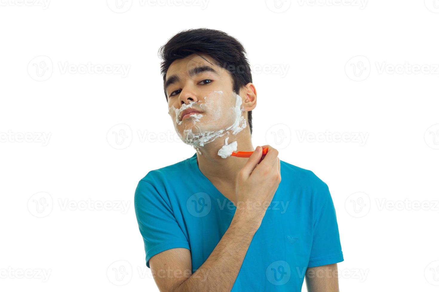 young guy with black hair looked up and shaves his beard with foam and machine photo
