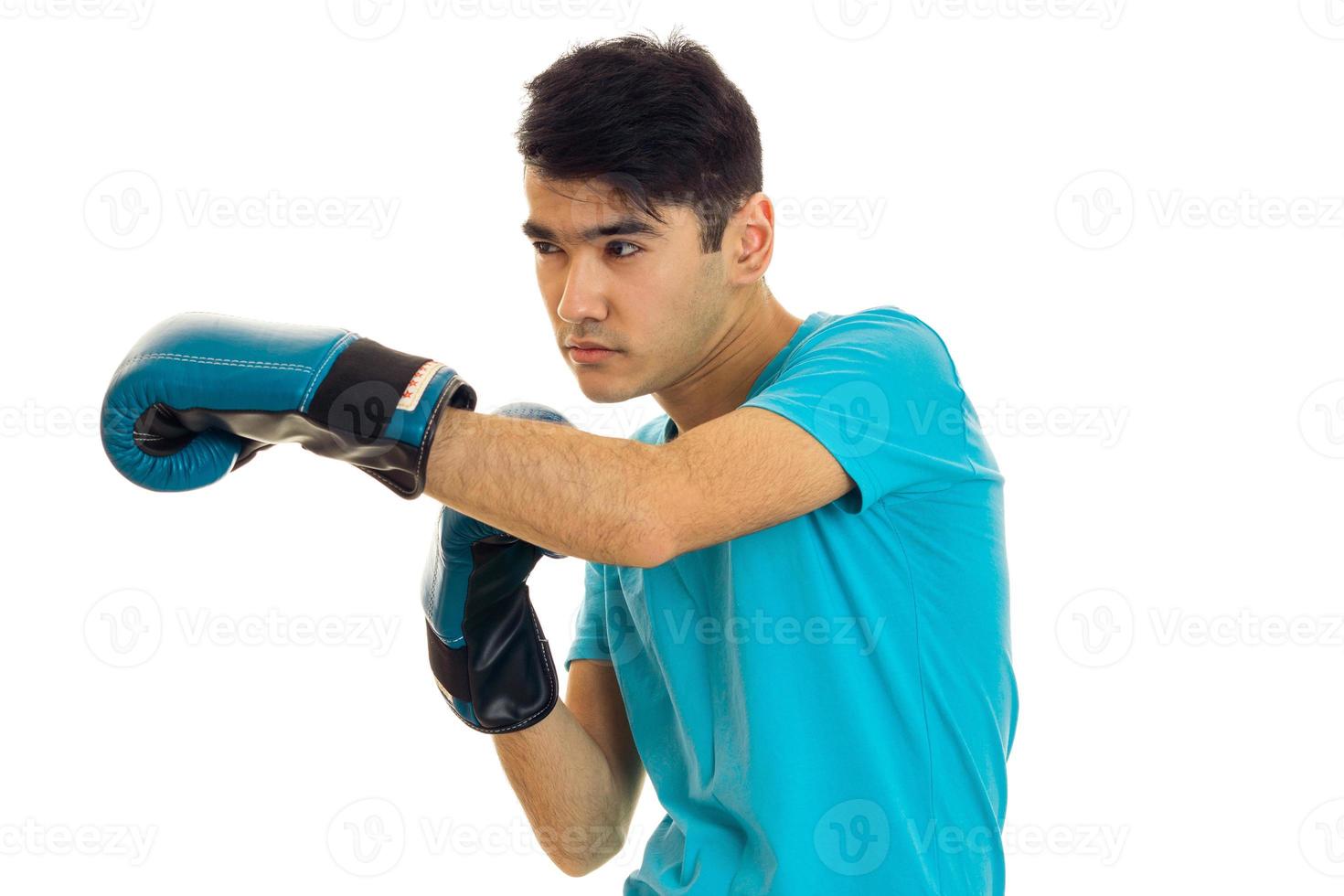 young serious brunette man in blue boxing gloves practicing isolated on white background photo