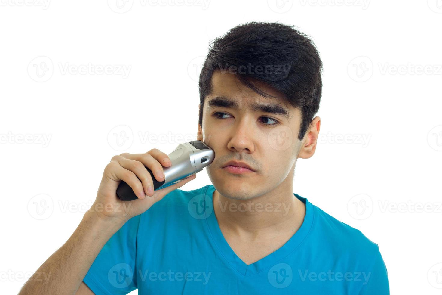 young strong guy in a t-shirt looking sideways and shaves a beard trimmer is isolated on a white background photo