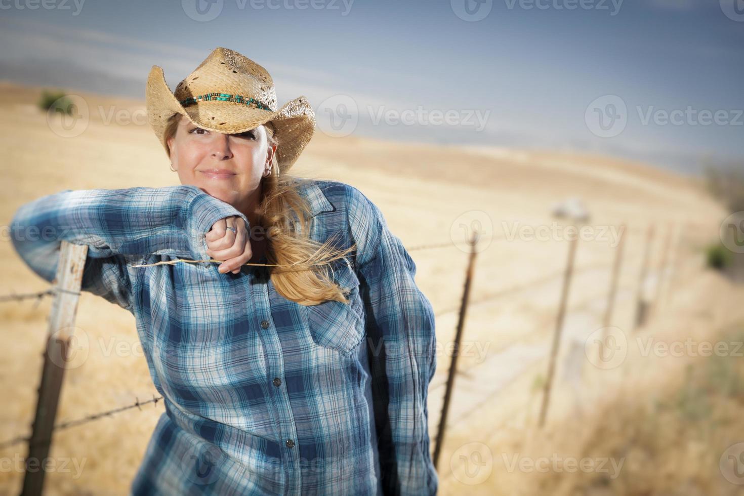 hermosa vaquera contra la valla de alambre en el campo foto