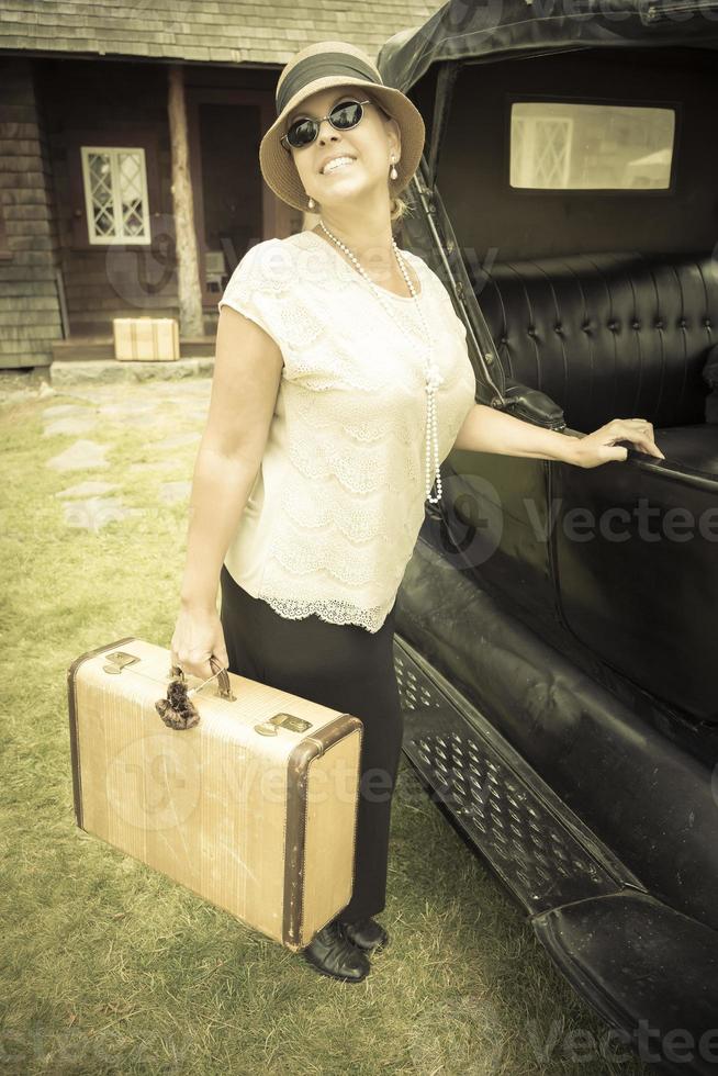 Happy 1920s Dressed Girl Holding Suitcase Next to Vintage Car photo