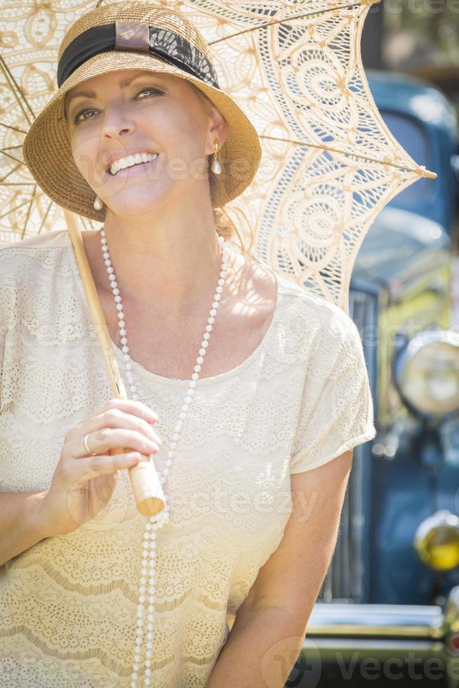 Niña vestida de los años 20 con sombrilla cerca del retrato de autos antiguos foto