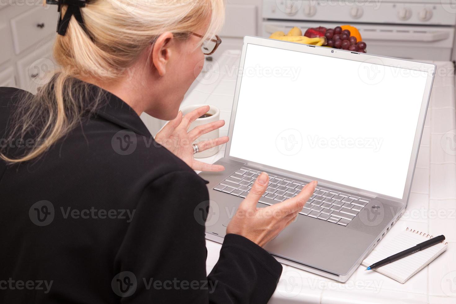 mujer emocionada en la cocina usando una laptop con pantalla en blanco foto