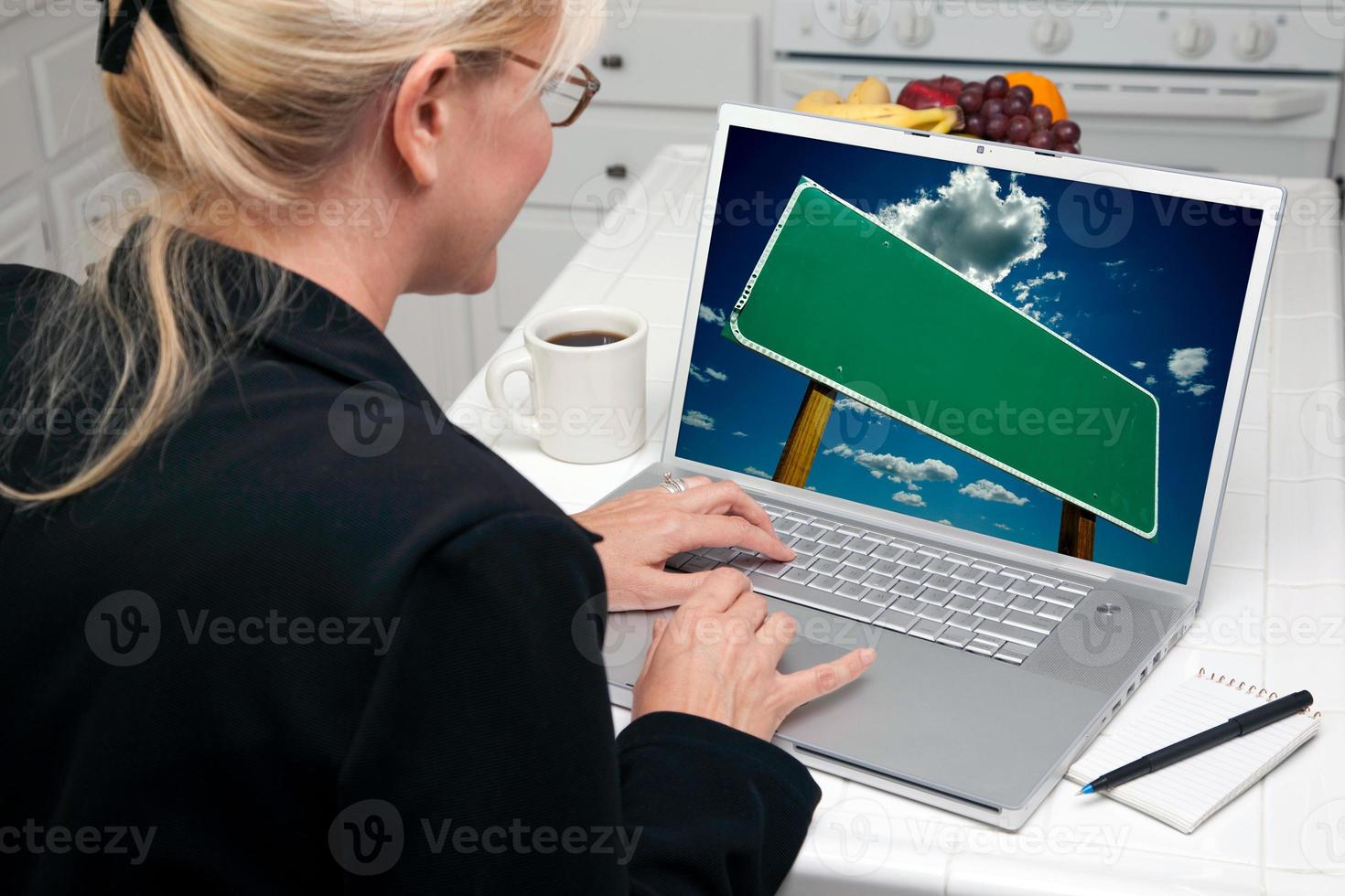 Woman In Kitchen Using Laptop with Blank Road Sign on Screen photo