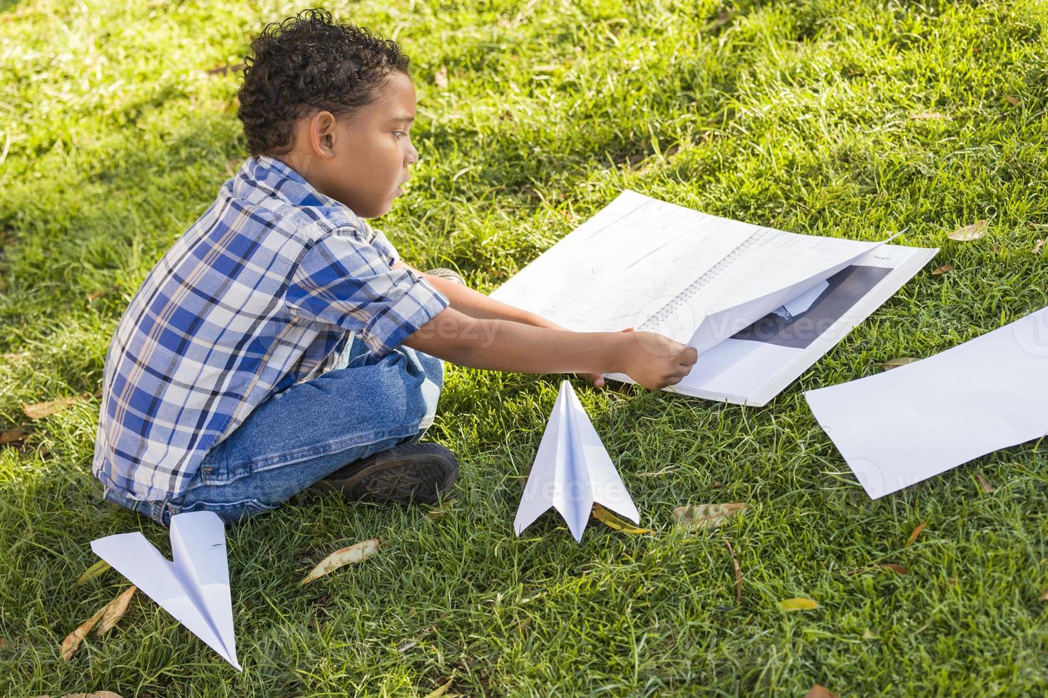 niño de raza mixta aprendiendo a doblar aviones de papel foto