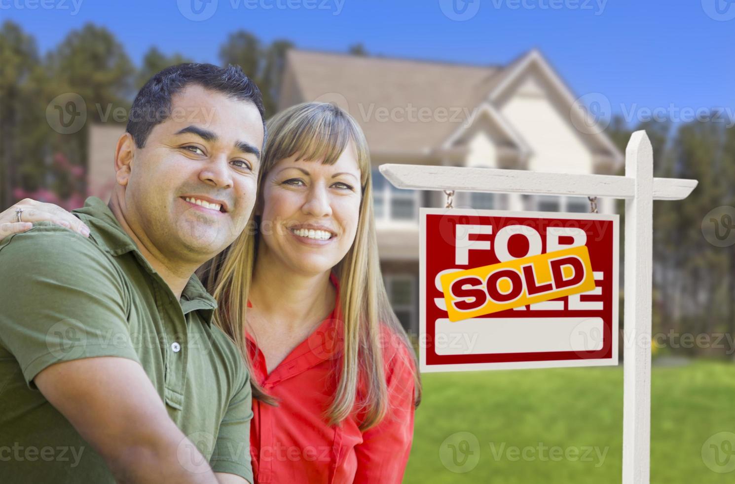 pareja frente al letrero de bienes raíces vendidos y la casa foto