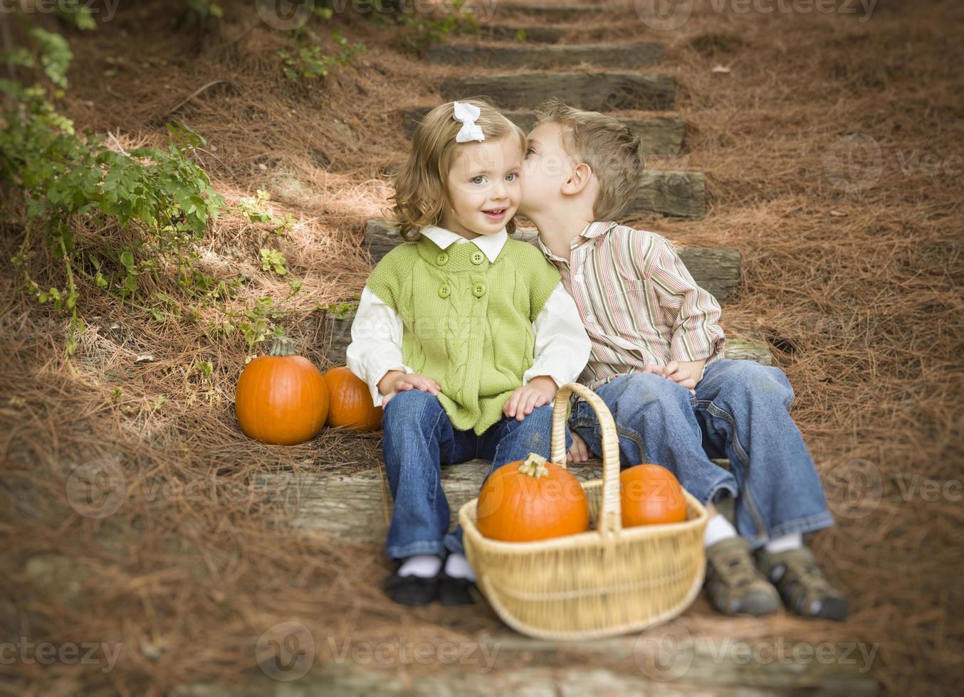 hermano y hermana niños en escalones de madera con calabazas susurrando foto