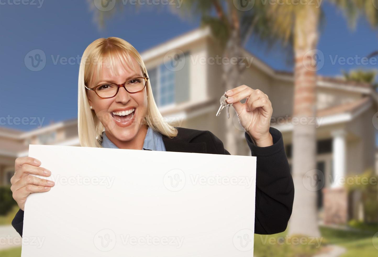 mujer emocionada sosteniendo las llaves de la casa y el cartel de bienes raíces en blanco foto