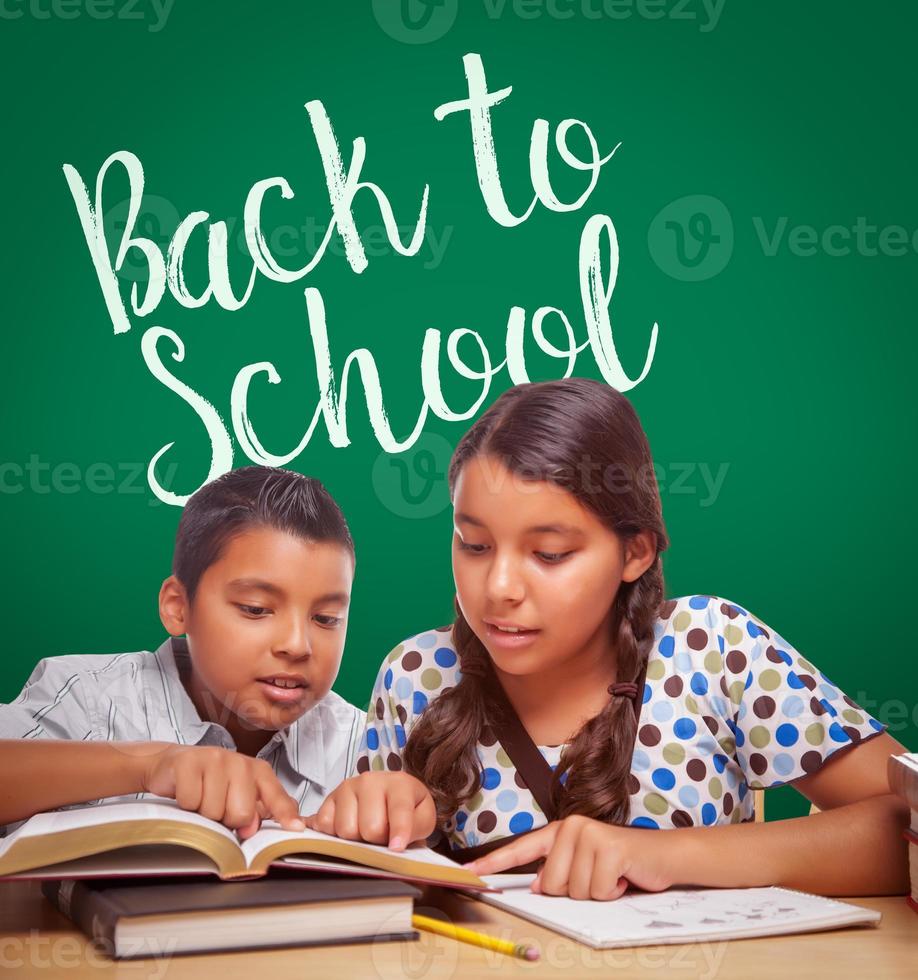 regreso a la escuela escrito en una pizarra detrás de un niño y una niña hispanos divirtiéndose estudiando juntos foto