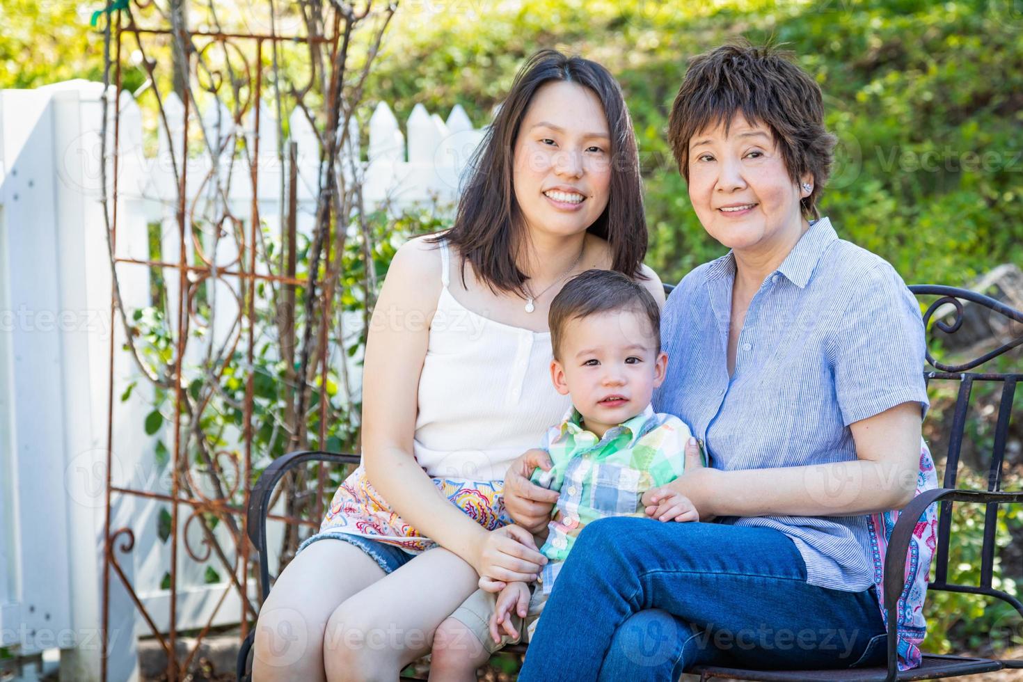 Chinese Grandmother, Daughter and Mixed Race Child Sit on Bench Outdoors photo