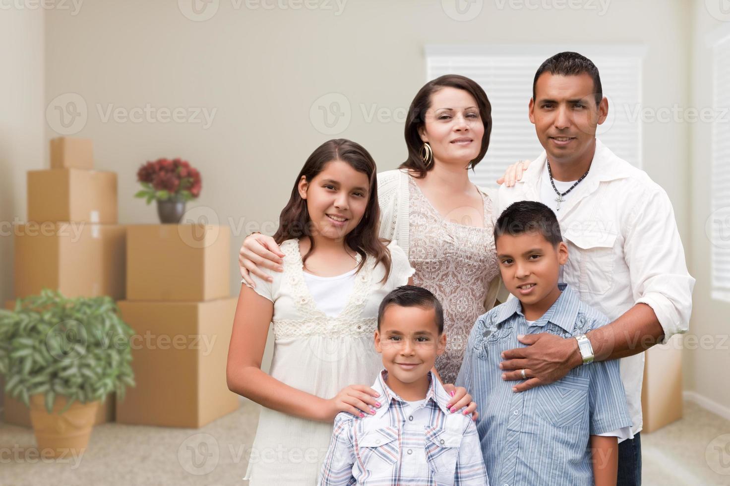 Hispanic Family in Empty Room with Packed Moving Boxes and Potted Plants photo