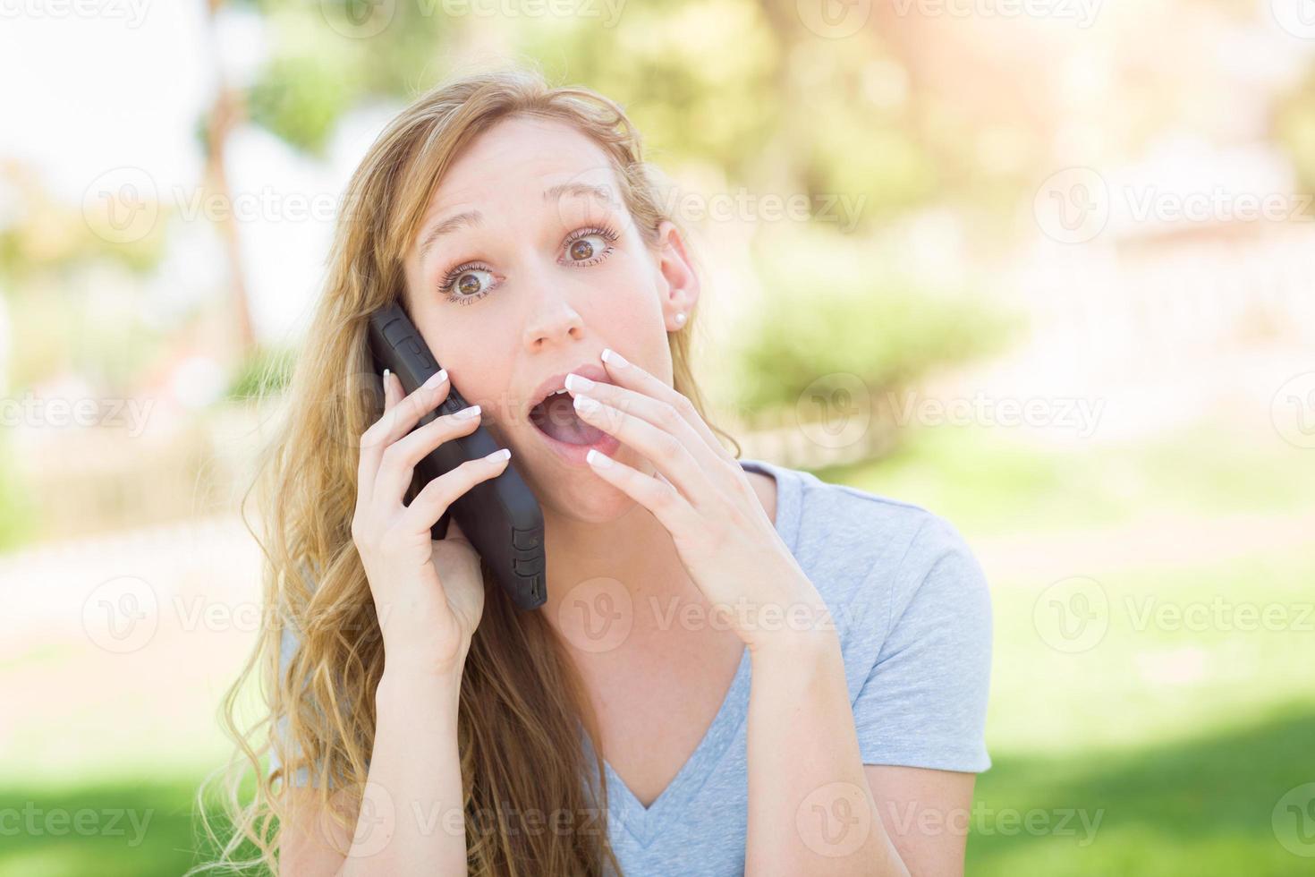 Stunned Young Woman Outdoors Talking on Her Smart Phone. photo