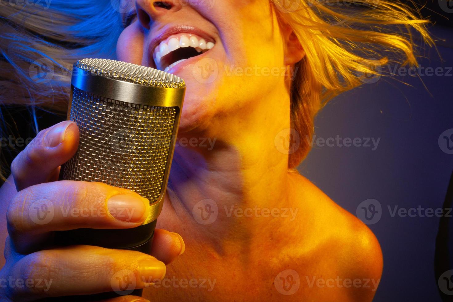 Female vocalist under gelled lighting sings with passion into condenser microphone. photo