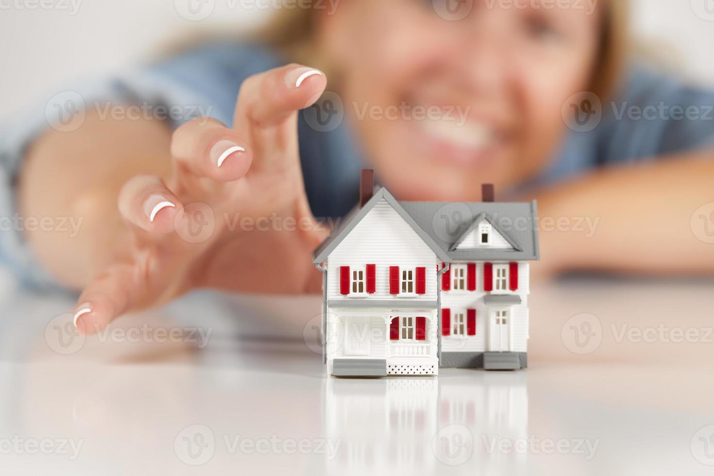 Smiling Woman Reaching for Model House on White photo