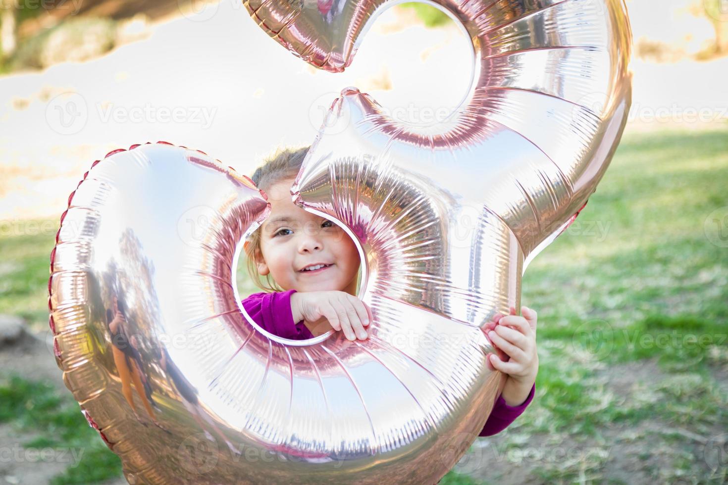 Linda niña jugando con globo mylar número tres al aire libre foto