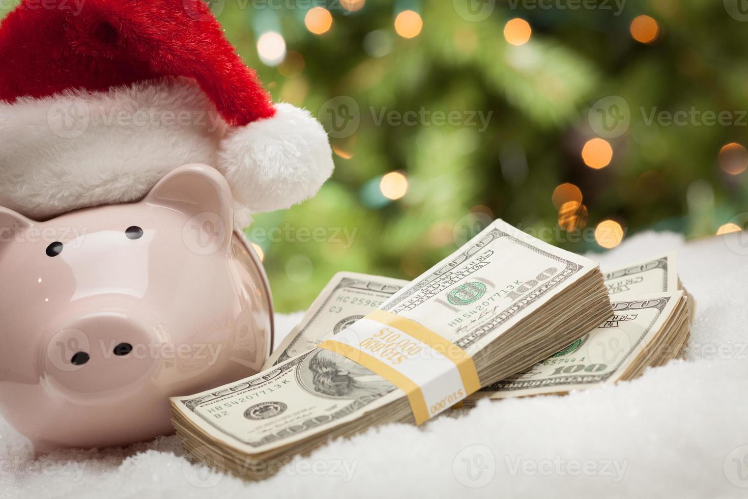 Piggy Bank Wearing Santa Hat Near Stacks of Hundred Dollar Bills on Snowflakes photo