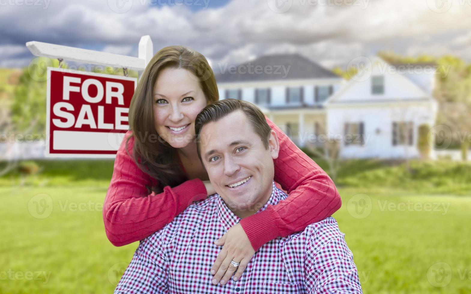 pareja feliz frente a la casa y el cartel de venta foto