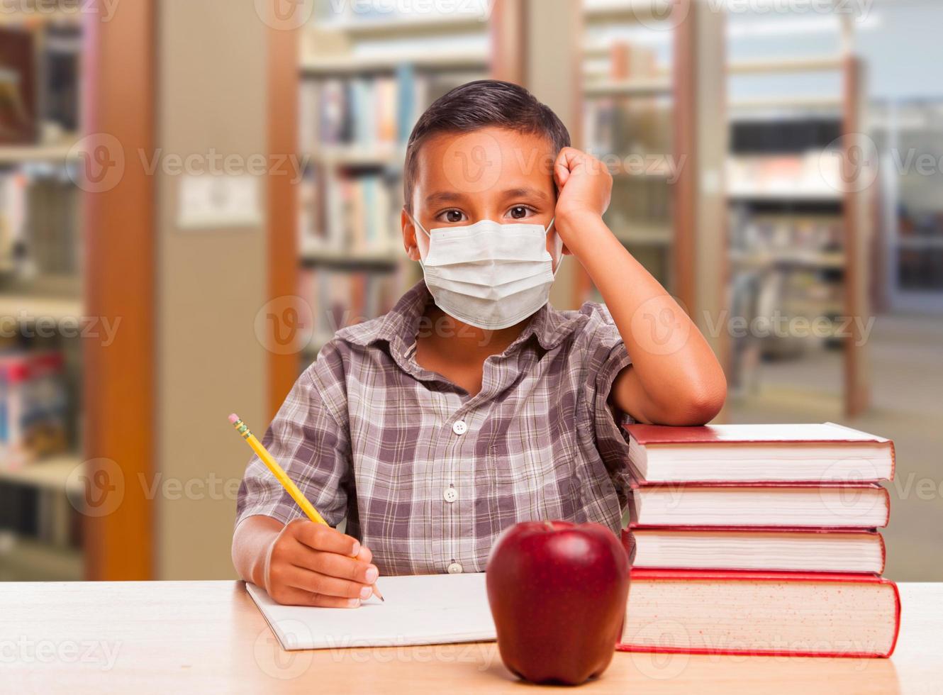 Hispanic Boy Wearing Face mask with Books, Apple, Pencil and Paper at Library photo