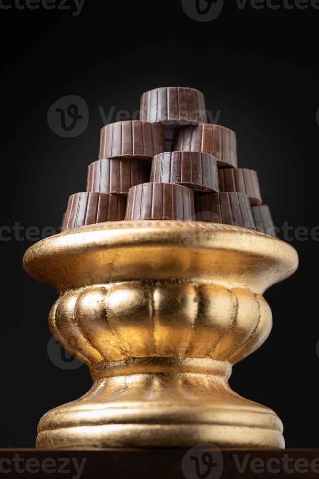 Stack of Fine Chocolates On Golden Pillar Dish With Dark Background photo