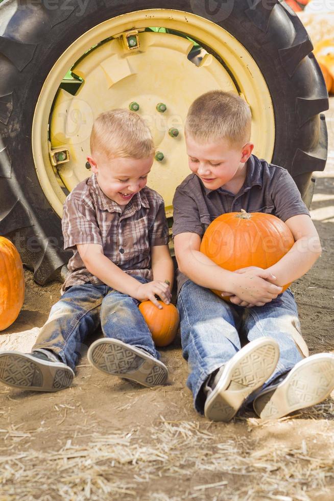 Two Boys Holding Pumpkins Talking and Sitting Against Tractor Tire photo