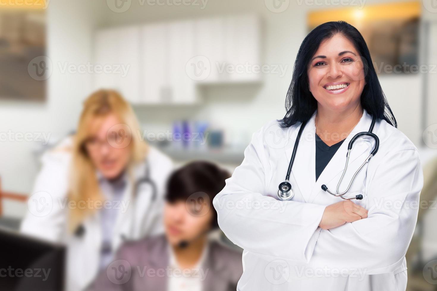 Handsome Hispanic Doctor or Nurse Standing in Her Office with Staff Working Behind photo