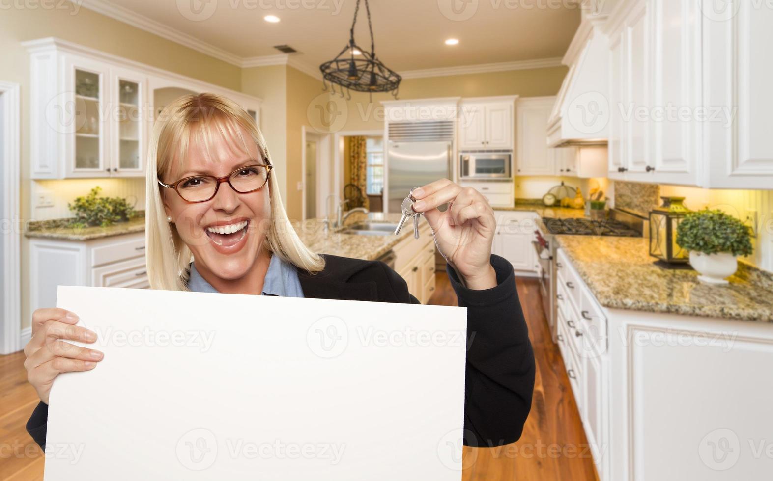 Young Woman Holding Blank Sign and Keys Inside Kitchen photo