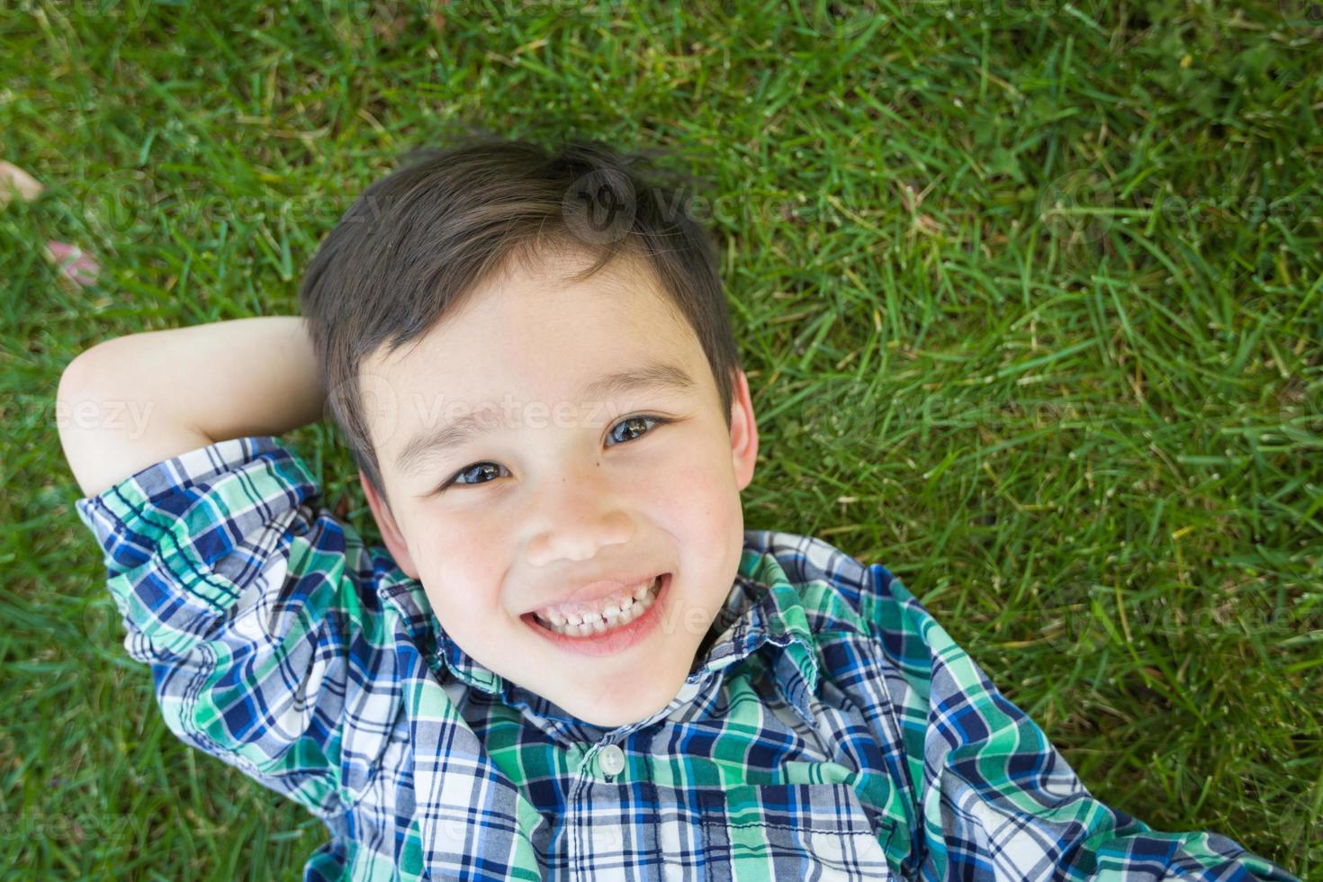 Mixed Race Chinese and Caucasian Young Boy Relaxing On His Back Outside On The Grass. photo