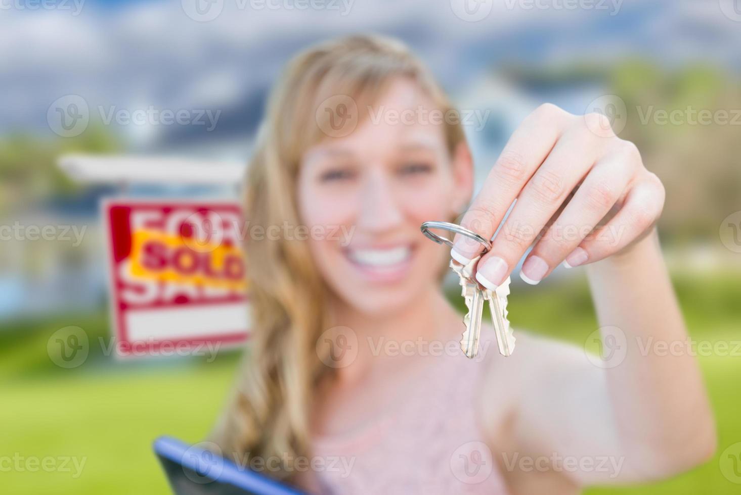 mujer emocionada sosteniendo las llaves de la casa y vendió el cartel de bienes raíces frente a una bonita casa nueva. foto