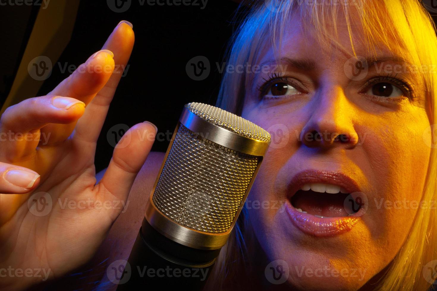 Female vocalist under gelled lighting sings with passion into condenser microphone. photo