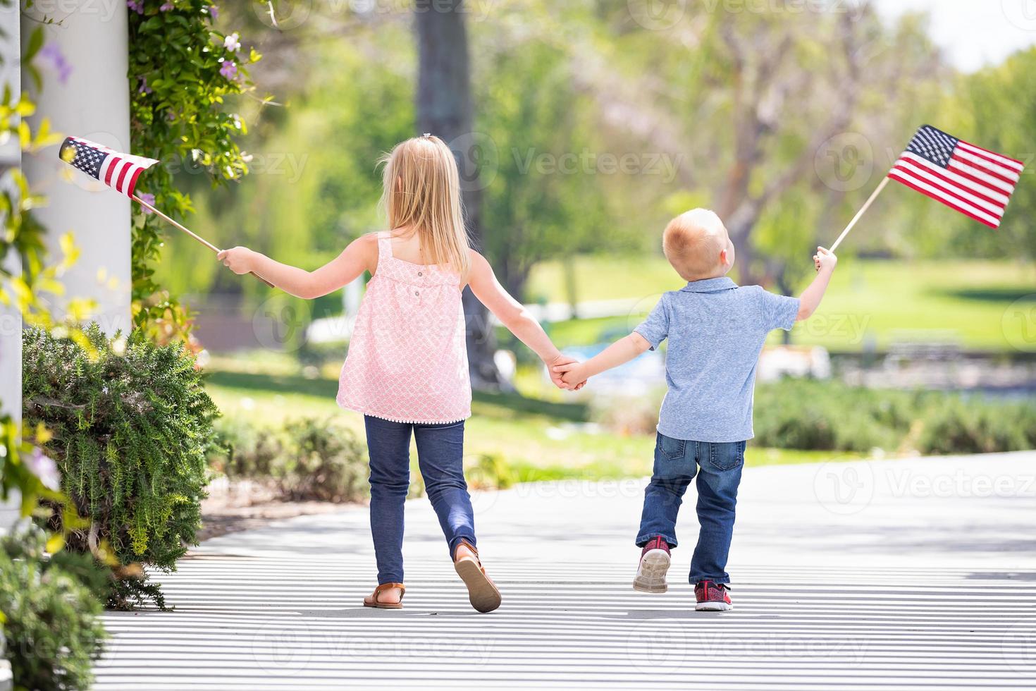 Young Sister and Brother Holding Hands and Waving American Flags At The Park photo