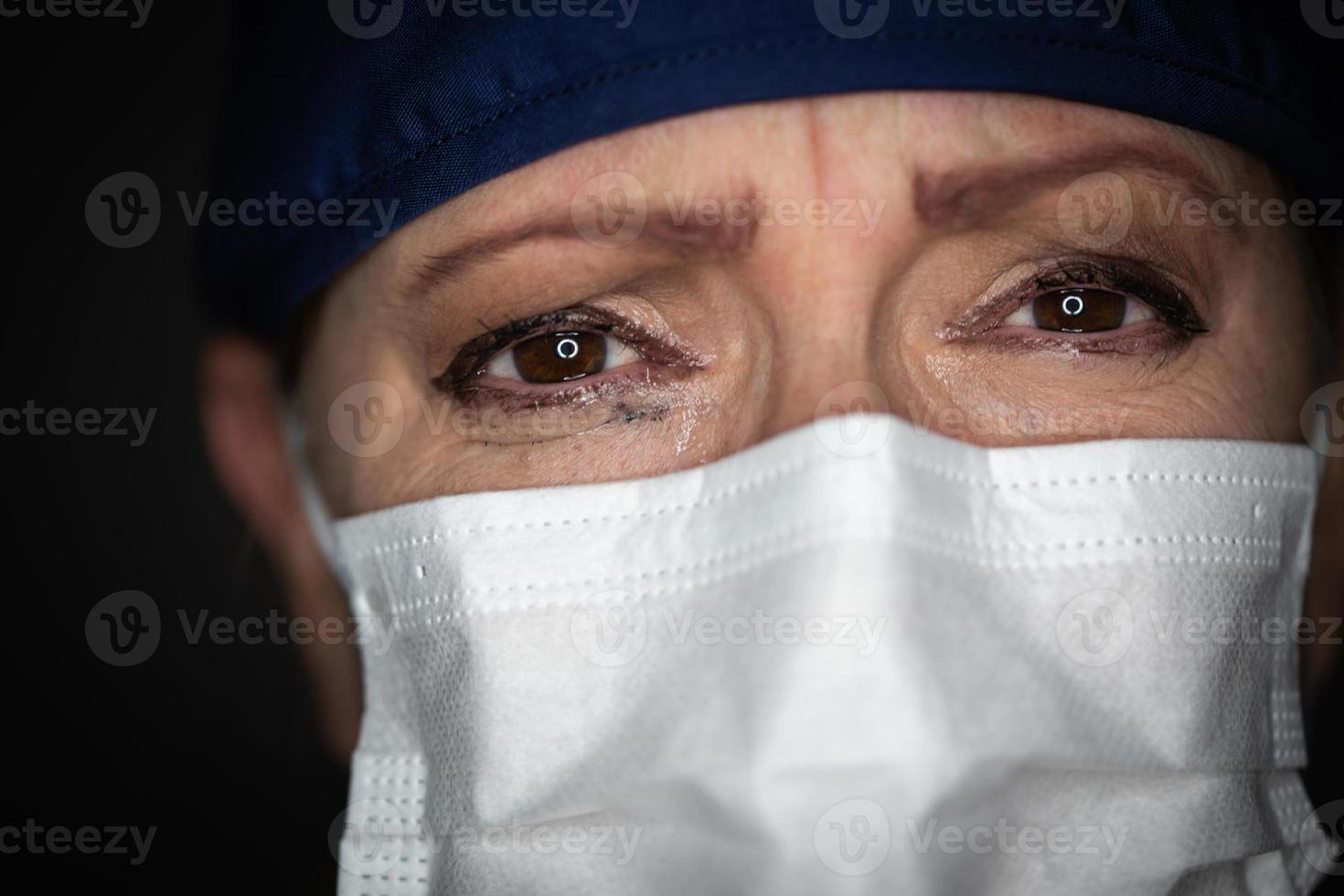 Tearful Stressed Female Doctor or Nurse Wearing Medical Face Mask on Dark Background photo