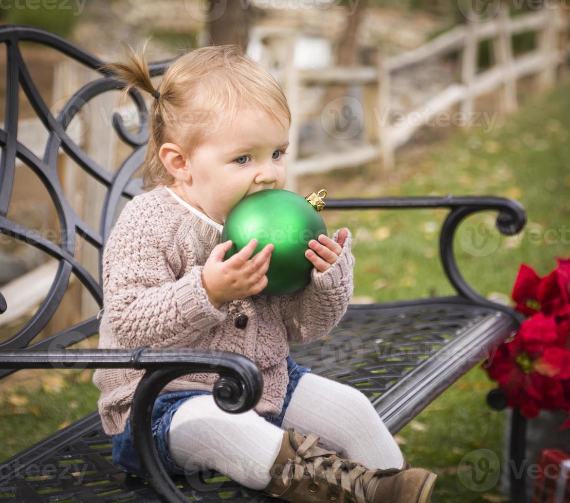 Toddler Child Sitting on Bench with Christmas Ornament Outside photo