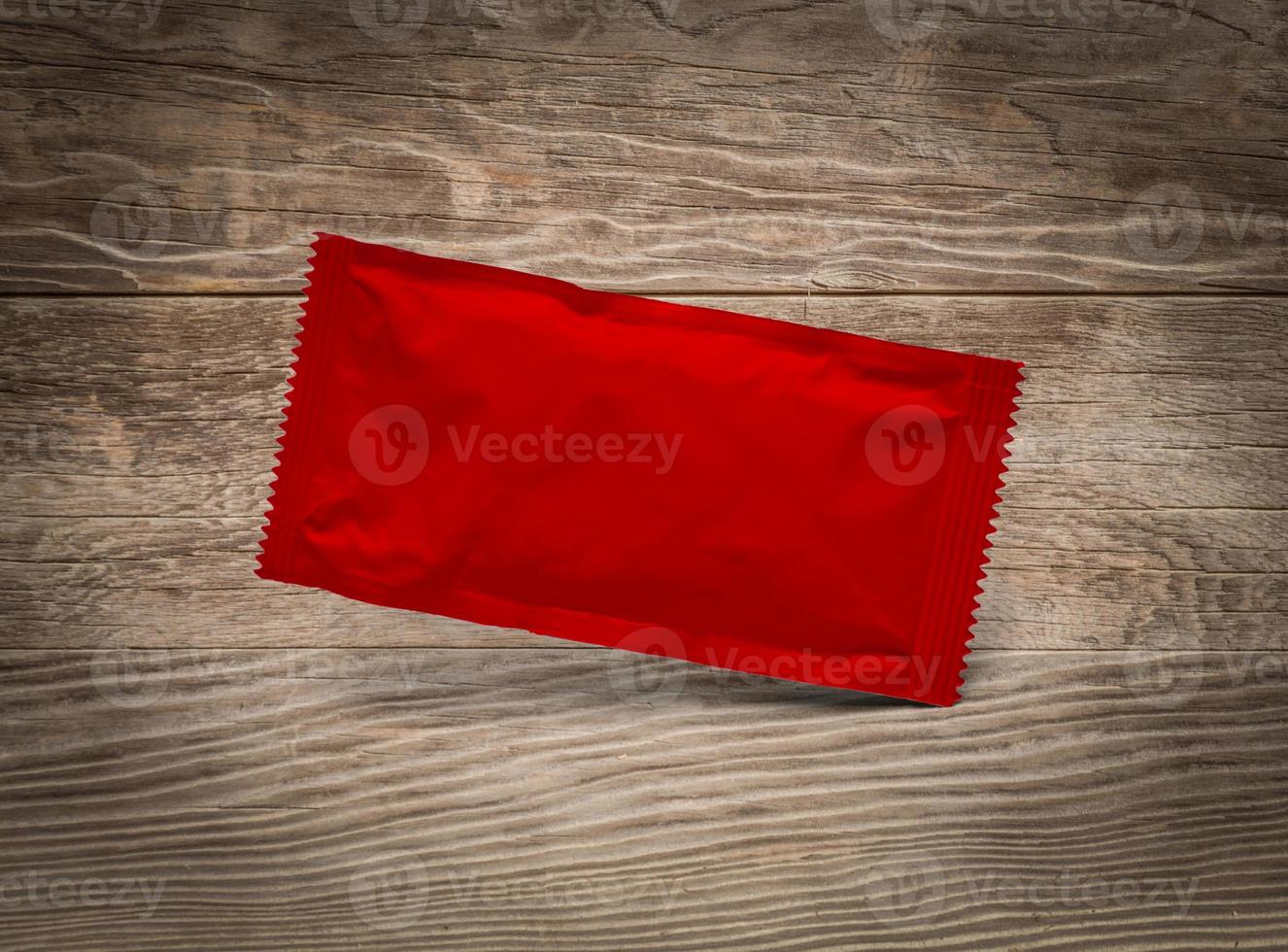 Blank Red Condiment Packet Floating on Aged Wood Background photo