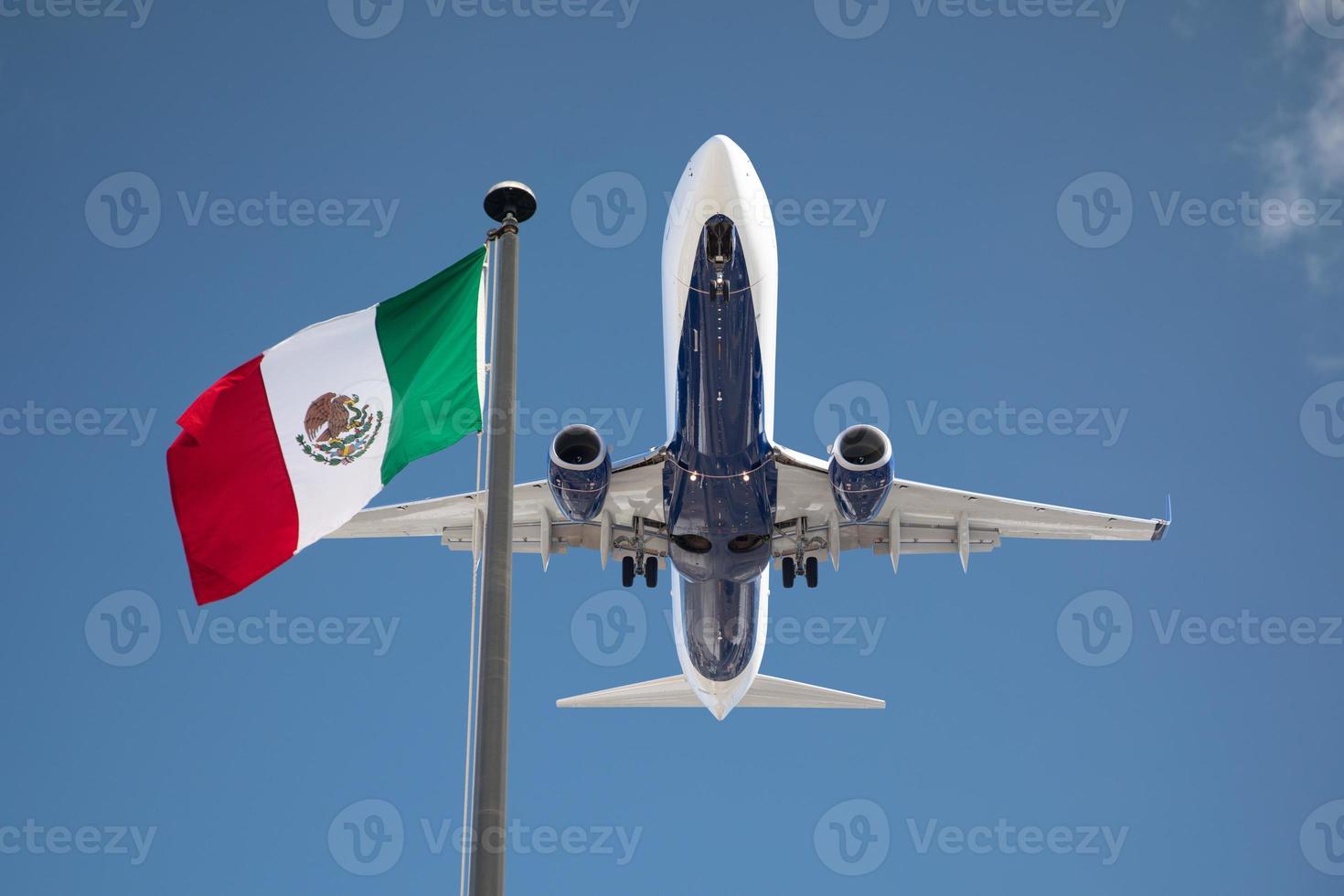 Bottom View of Passenger Airplane Flying Over Waving Mexico Flag On Pole photo