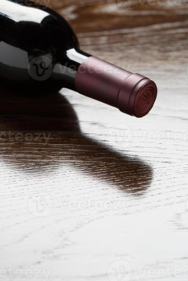 Red Wine Bottle Laying on a Wood Surface Fading Down to White. photo