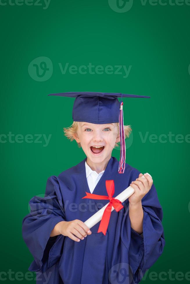 Cute Young Caucasian Boy Wearing Graduation Cap and Gown Against Blank Green Background photo