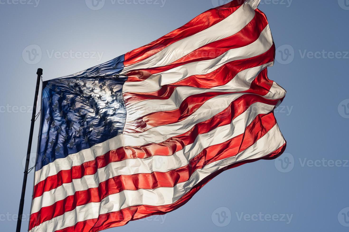 bandera americana retroiluminada ondeando en el viento contra un cielo azul profundo foto