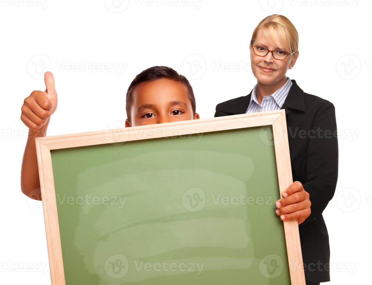 niño hispano sosteniendo una pizarra y una maestra detrás foto