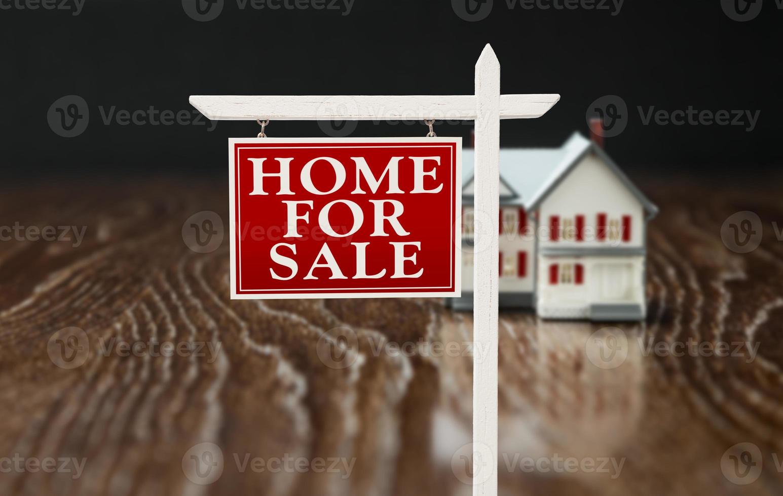 For Sale Real Estate Sign In Front of Model Home on Reflective Wooden Surface. photo