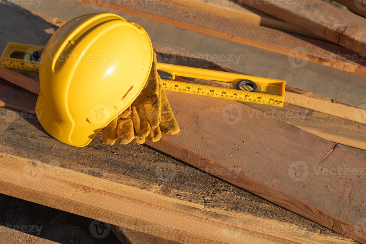 resumen de la construcción de cascos, guantes y nivel descansando sobre tablones de madera foto