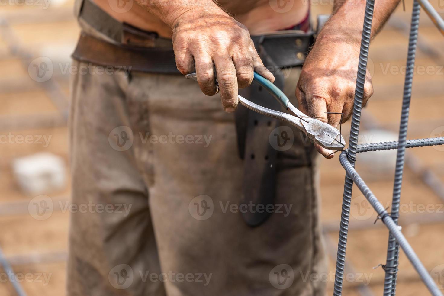 Worker Securing Steel Rebar Framing With Wire Plier Cutter Tool At Construction Site photo