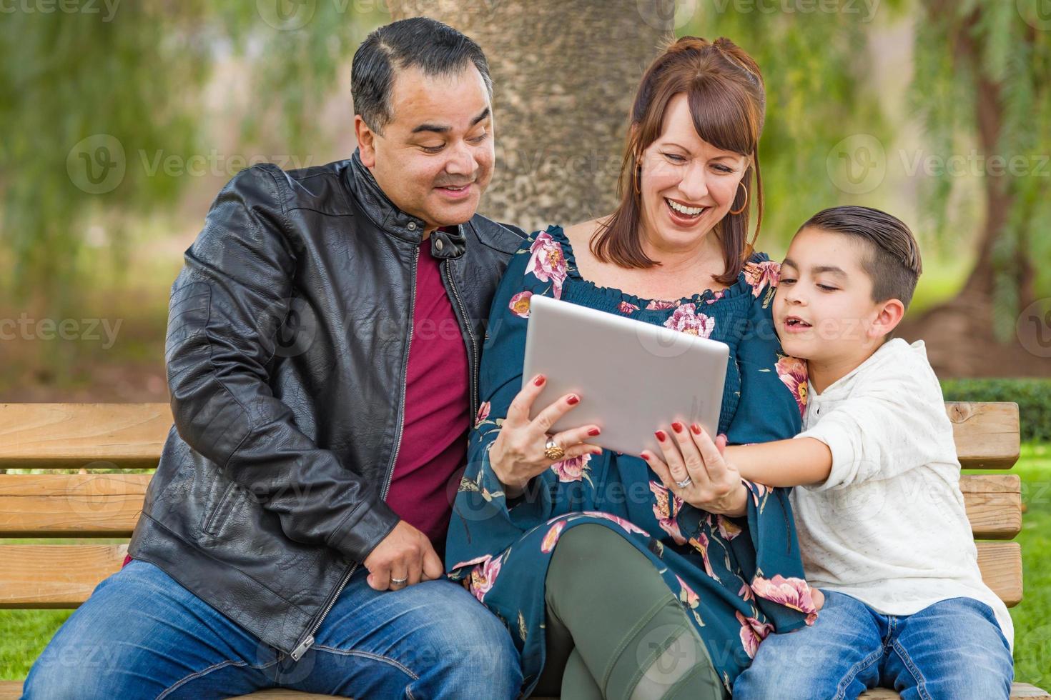 madre caucásica y padre hispano usando tableta de computadora con hijo de raza mixta al aire libre foto