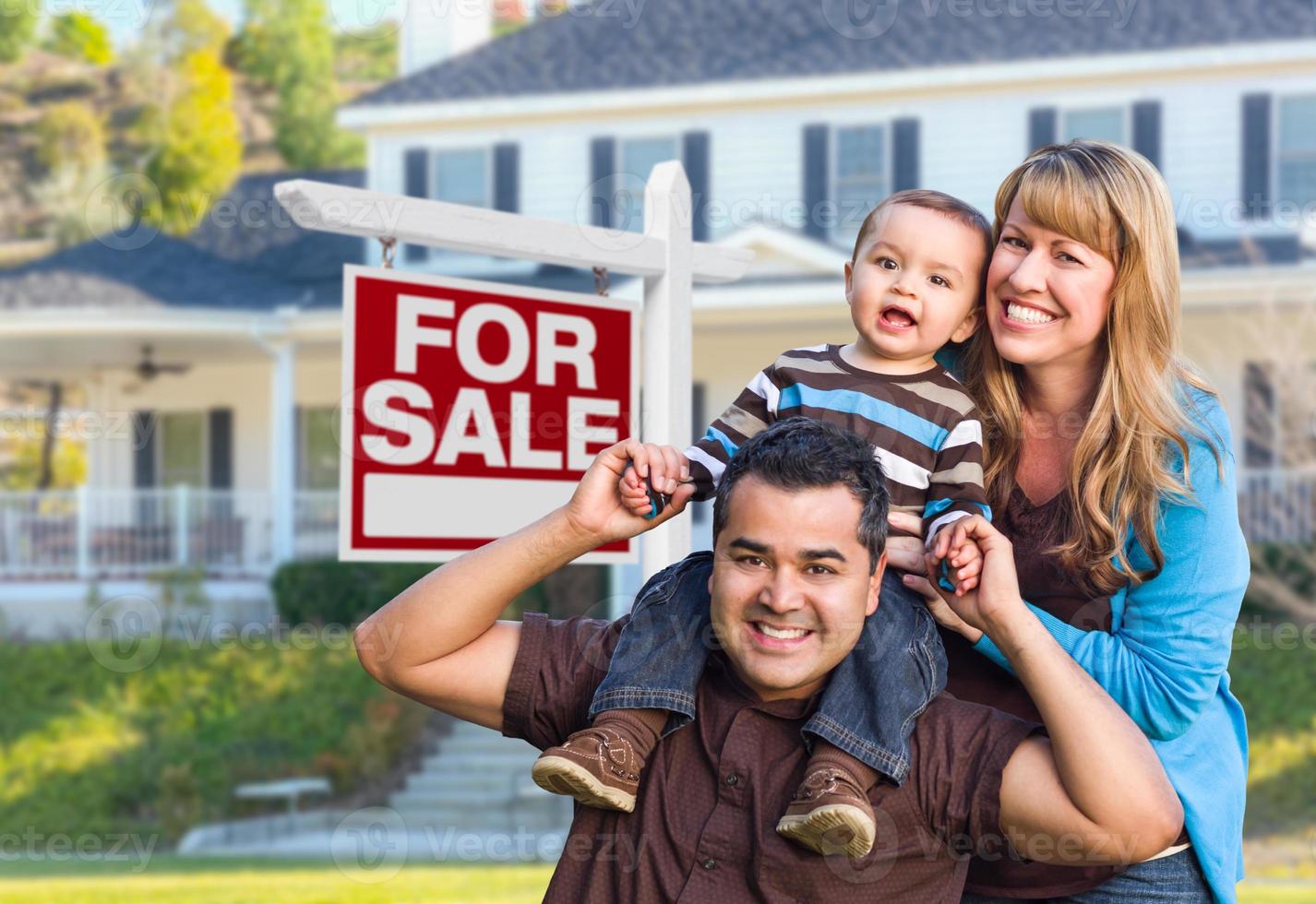 familia joven frente a la casa y el cartel de venta foto