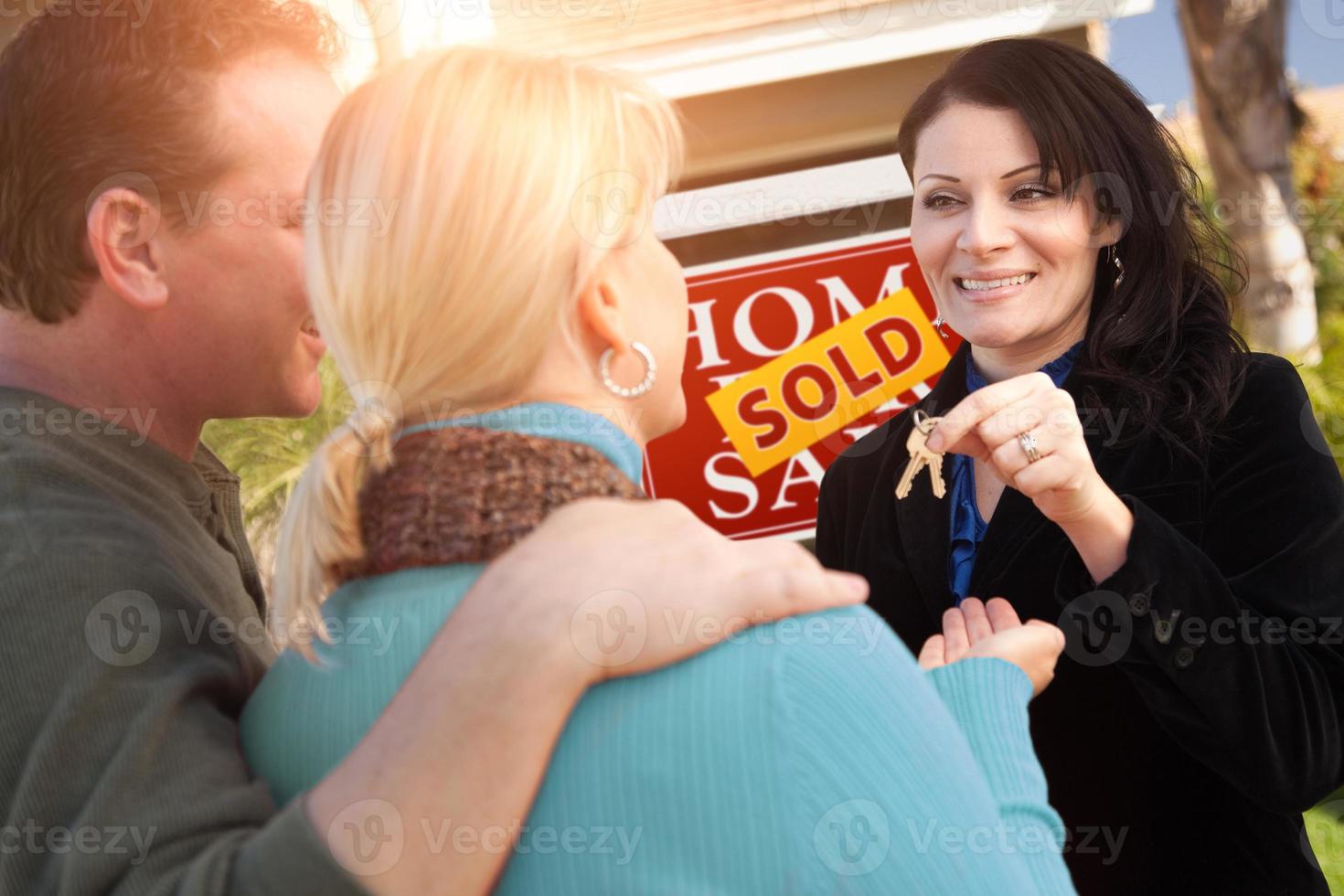 agente inmobiliaria hispana entregando las llaves de la nueva casa a una pareja feliz frente al cartel de bienes raíces vendidos en venta foto